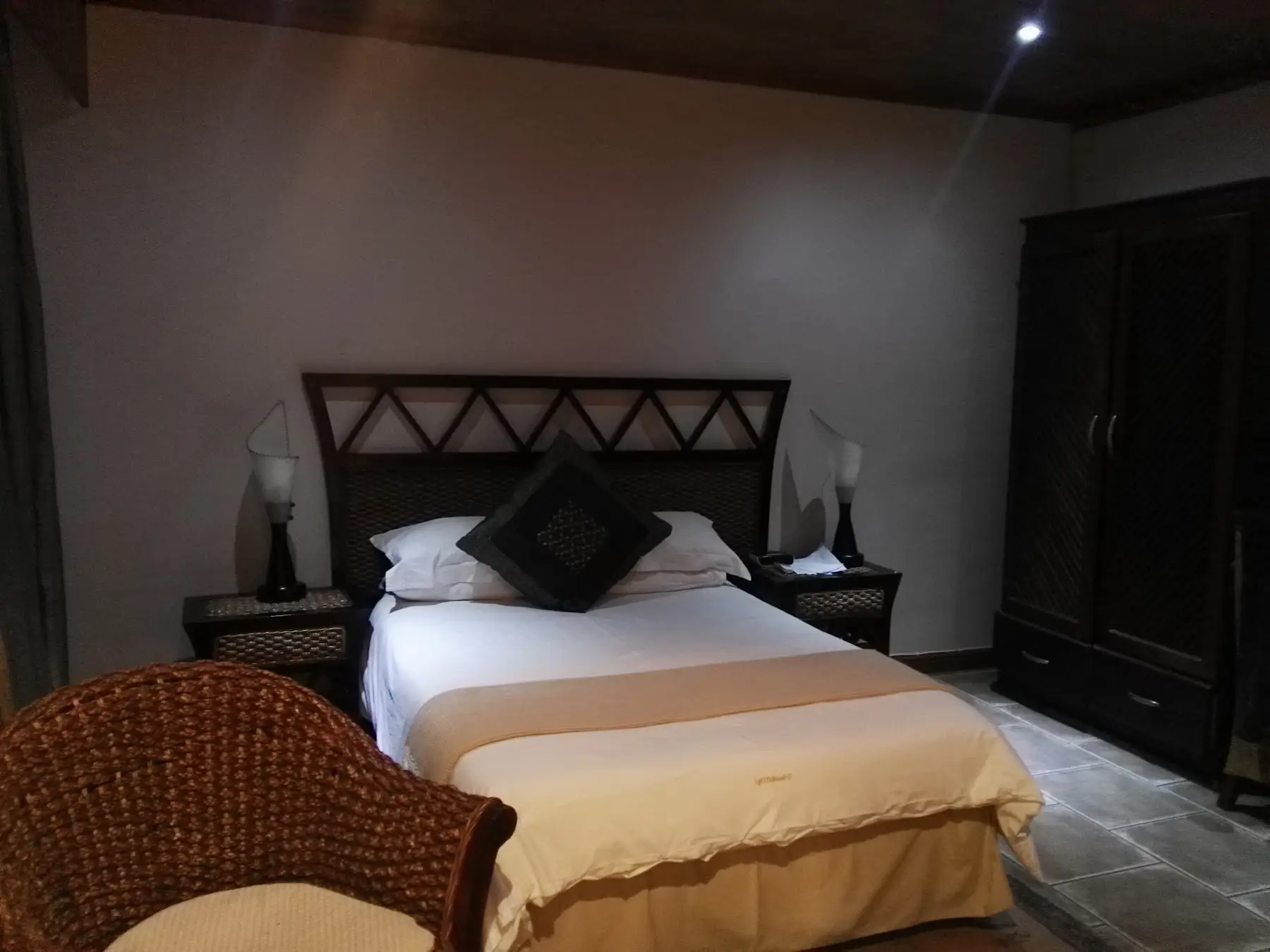 A double room: a lattice headboard, wicker chair and dark wood