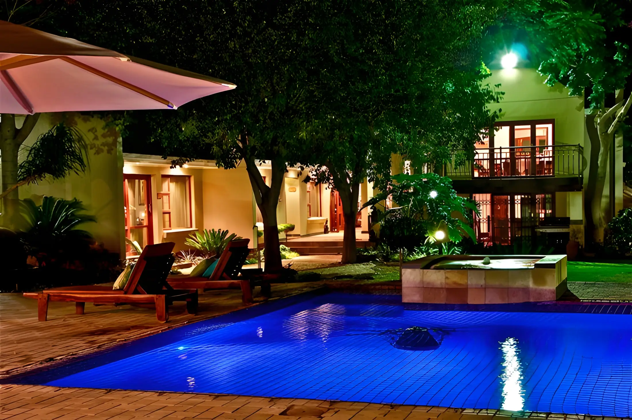 The pool lit blue at night, loungers and the house beyond